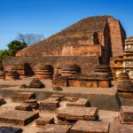 नालंदा महाविहार के प्राचीन ईंट-निर्मित खंडहर, जिनमें एक विशाल मंदिर संरचना, छोटे स्तूप और पुरातात्विक अवशेष साफ़ नीले आकाश के नीचे दिखाई दे रहे हैं।